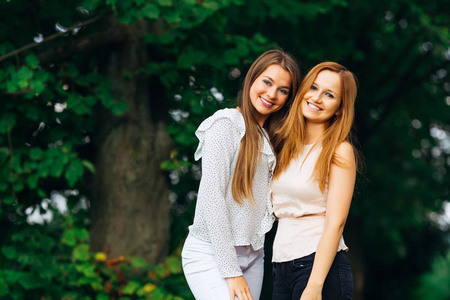 两个漂亮的女孩穿着时髦的衣服看相机镜头和微笑的背景公园