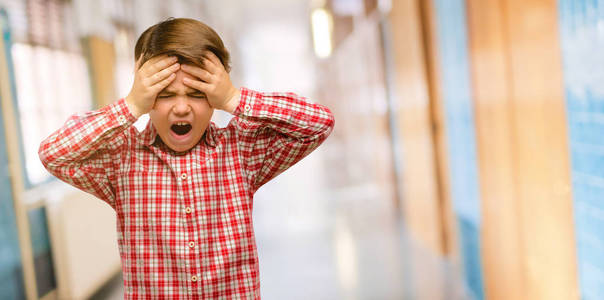 眼睛的英俊的小孩, 紧张得双手牵着头, 惊恐万分, 在学校走廊大喊大叫
