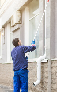一个年轻的男性清洁工在蓝色工作服洗涤窗口和商店前面。清洁服务