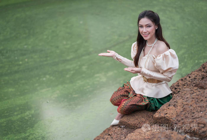 在泰国传统礼服在池塘附近的愉快的美丽的妇女