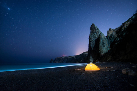 在下一个繁星满天的夜晚发光与岩石的美丽海边露营帐篷照片