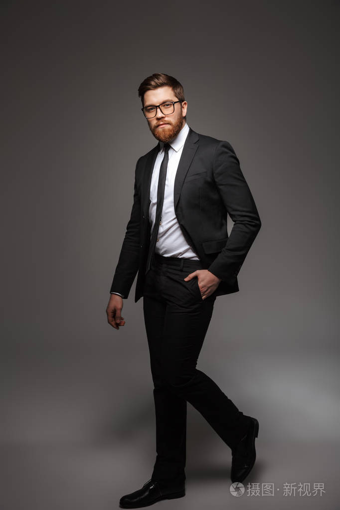 一个充满自信的年轻商人穿着西装走在灰色背景下行走的全长肖像