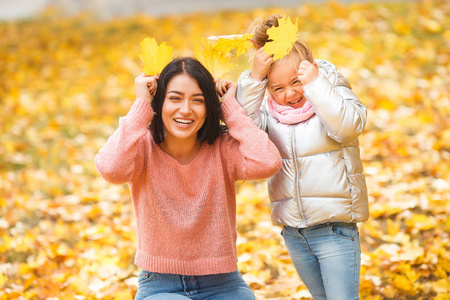 欢快的女孩玩黄叶。快乐的母亲和小孩子在秋天的时间有乐趣