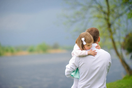 父亲带着小女儿走在河岸上, 女孩温柔地与爱拥抱着父亲.照片