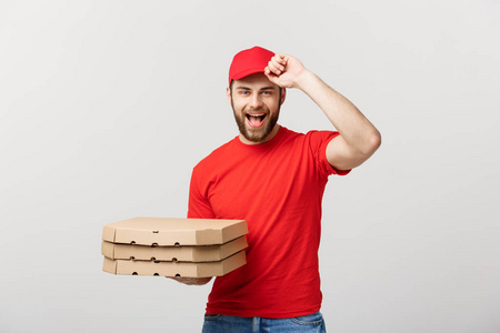 送货理念 英俊的比萨饼送货员身着红色制服, 上面夹着比萨饼盒。在白色上隔离