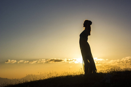 silhouete 在夕阳山上的草地上穿衣的女孩