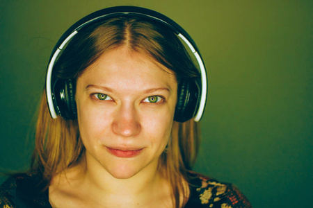 绿色眼睛的女孩听音乐与耳机在绿色背景下