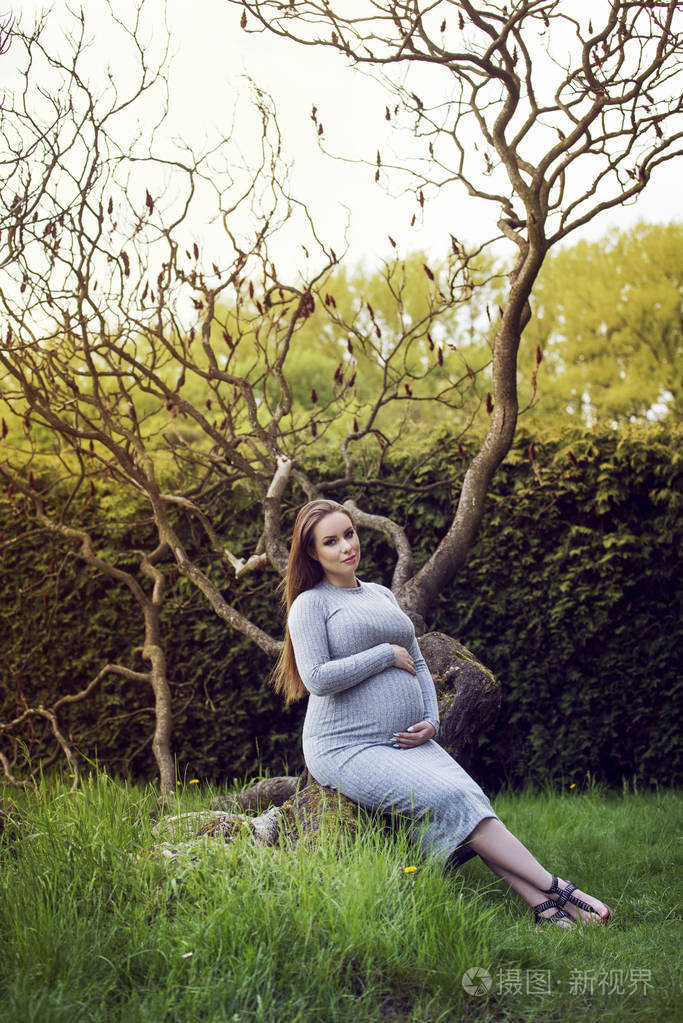 美丽的孕妇坐在一棵树下的公园