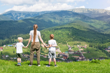 母亲和两个儿子站在那里欣赏着山的景色.后退视图.阳光明媚的夏日照片