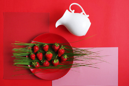 明亮的红色草莓和一个红色的背景奶油白色水罐。顶部视图