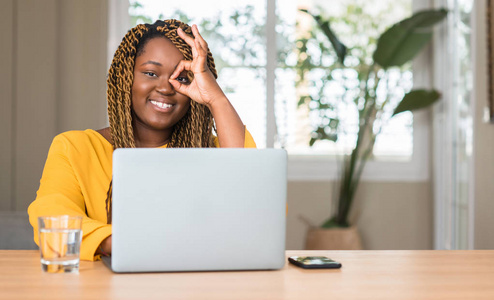 非洲裔美国妇女与膝上型电脑愉快的面孔微笑做 ok 标志用手在眼睛看通过手指