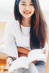 微笑的妇女读书书在木椅子在图书馆, 教育概念