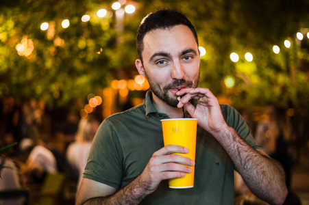 英俊的胡子欧洲人喝 coctail 或啤酒在户外街道咖啡馆夜间聚会在公园