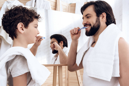 快乐的父亲和儿子用牙刷刷牙, 看着镜子