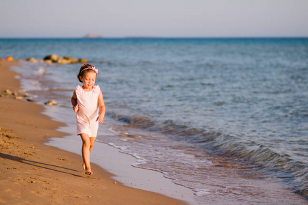在日落时分在海滩上奔跑的粉红色连衣裙的小女孩.在运动中查看.