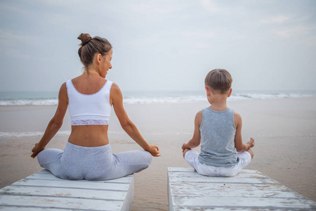 一位母亲和儿子正在做瑜伽练习在热带海洋的海滨