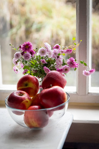 在一个透明的碗和窗台上的花朵的红色苹果的农村静物