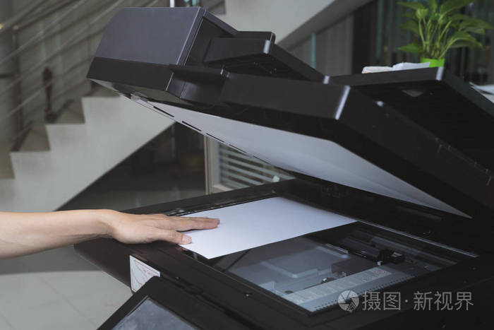 妇女手把一张纸放进办公室的复印设备中