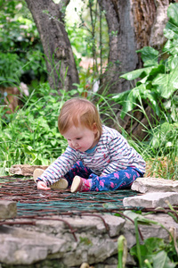 美丽的婴孩坐, 微笑和摆姿势, 画像。小可爱的女孩在花园里嬉戏。孩子在公园外面玩耍, 四周是美丽的绿树和灌木, 自然环境