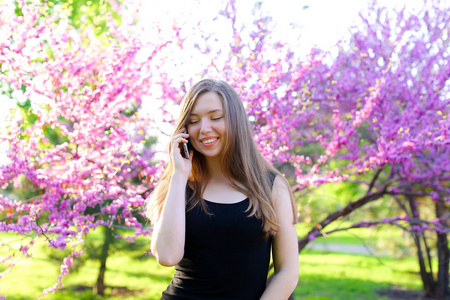 微笑的女孩走在春天公园和智能手机交谈