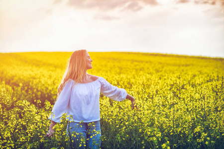 微笑的女士在日落时分走在黄色油菜花田