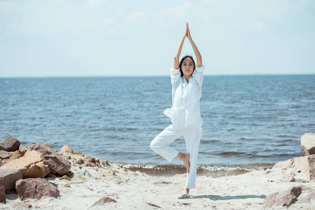 亚洲女子站在海边的 vrikshasana 树姿 上的前景色