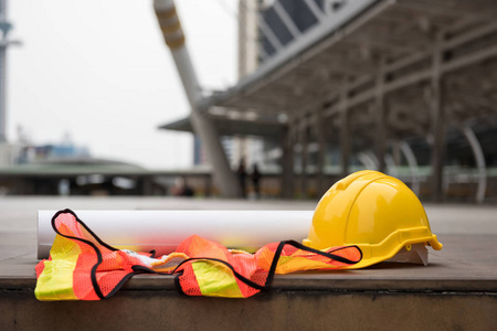 安全黄色头盔帽子, 蓝图纸项目, 和工人礼服在混凝土地板上的现代城市与模糊的人。具有复印空间的工程师和建筑设备