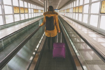 在自动人行道上国际航空手提行李的年轻女子