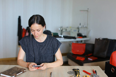 创意 craftswoman 坐在画室和使用智能手机, 手工皮革制品