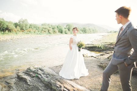 新娘和新郎抱着美丽的婚礼花束。河边摆姿势