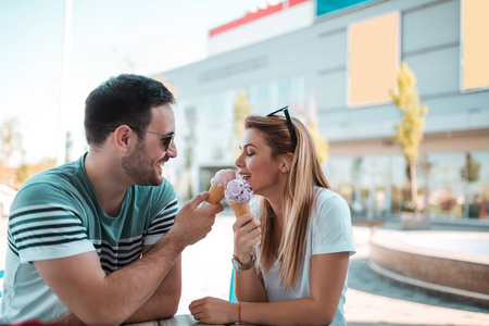 快乐的年轻夫妇坐在购物中心前吃冰淇淋