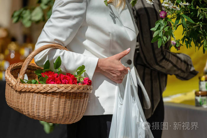 穿着白夹克的女人把一篮子花放在她的胳膊肘上。