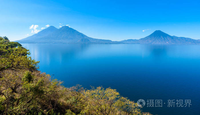 从湖阿特蒂兰湖的看法在清晨, 蓝色天蓝和清澈的水, 美丽的魔法湖与火山和土著居民在危地马拉高地图片采取接近巴哈契最旅游城市那里