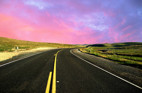 色彩斑斓的天空和云旅游概念在空的沥青路面，通过绿色的田野上行驶