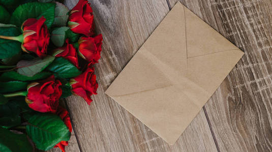 束红玫瑰与信封和为您的文本的空白纸卡木制的桌子上