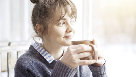 年轻美丽的女人穿着灰色的毛衣是享受她的茶在咖啡馆和白日梦