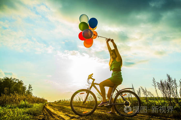 年轻女孩在性感的礼服骑自行车飞行空气气球