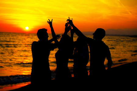 日落时海滩派对上年轻人的剪影