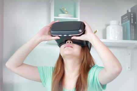在家里戴着虚拟现实眼镜的年轻女子。虚拟现实耳机是一个头部安装的设备, 提供虚拟现实的佩戴者