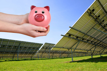 太阳能电池板和小猪银行手中。节约能源的概念