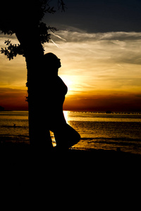 一个女人靠在海滩上欣赏日落的树的剪影照片