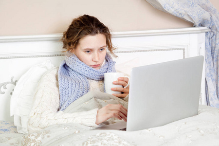 生病的女人感觉不好，休息和工作与她的手提电脑和互联网在她家里的床上
