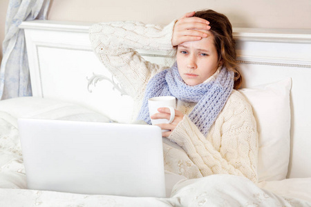 生病的女人感觉不好,休息和工作与她的手提电脑和互联网在她家里的床
