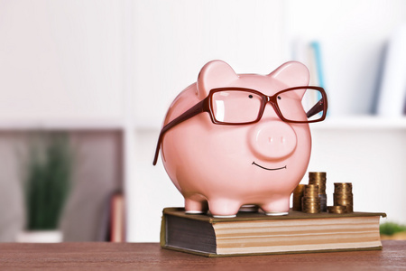 储钱罐在眼镜与书和在家里或办公室的背景上的硬币照片