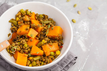 小扁豆与南瓜烩在一个白色的碗上灰色的背景。健康素食概念