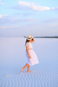 穿着白色礼服和帽子的年轻女孩赤脚去沙