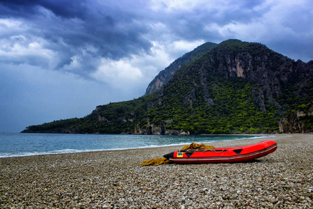 壮观的山的风景与红色小船在海附近与石海滩和蓝色天空。Olympos 海滩, 土耳其