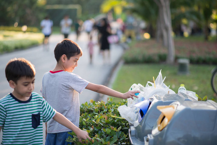 以垃圾到垃圾桶在公园里的小男孩照片