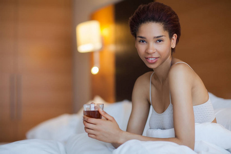 快乐的年轻黑人妇女坐在床上，喝中国茶