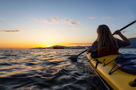一只独木舟上的女人在 paddeling 的日落时被大海所影响。在加拿大不列颠哥伦比亚省温哥华拍摄